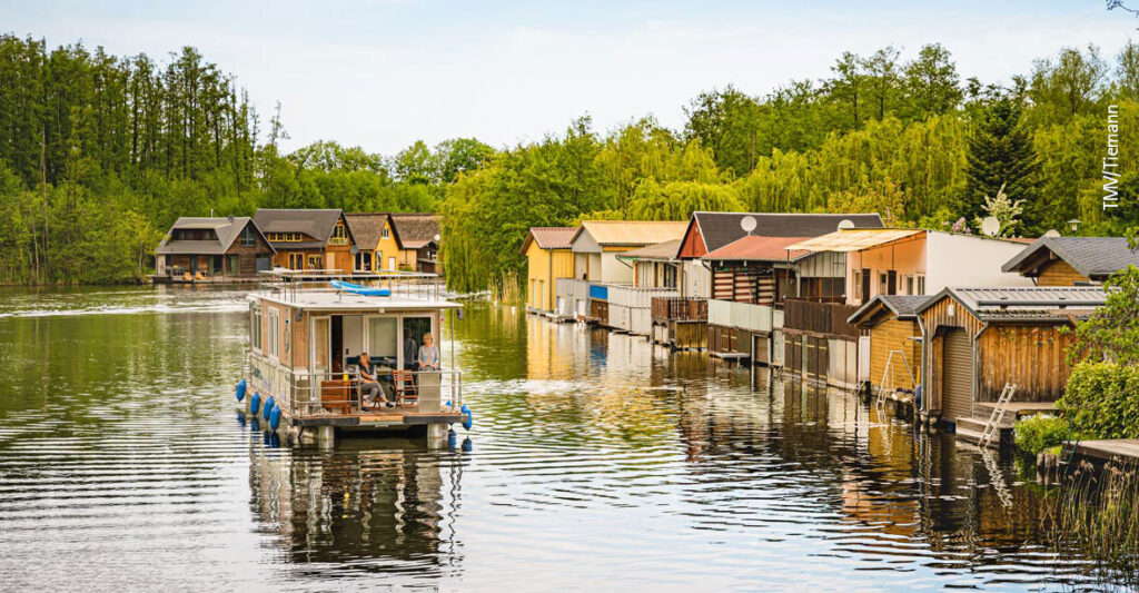 Das Saunahausboot fährt an einer Reihe Bootshäusern vorbei.