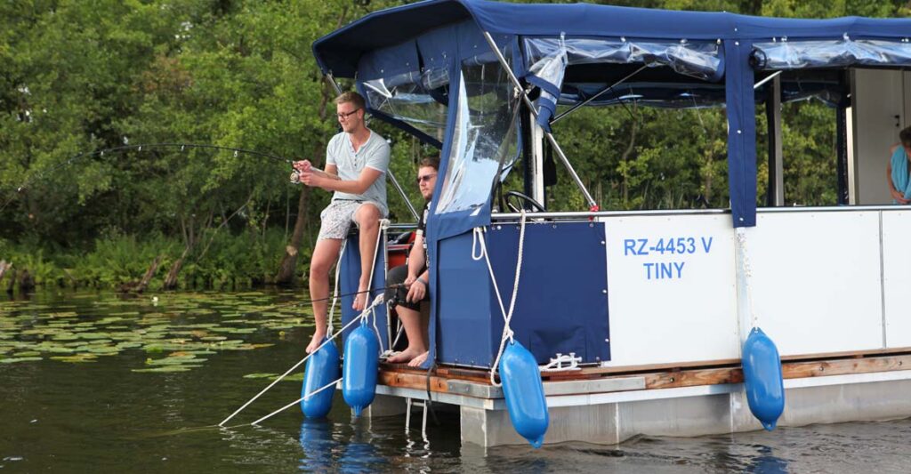 Zwei Männer sitzen auf dem Febo720 open und Angeln. Einer sitzt auf der Reling, der andere auf einem Stuhl.