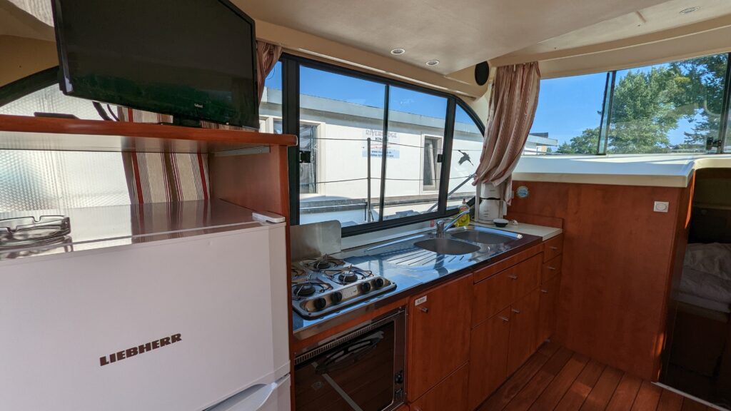 Küchenzeile mit Spülbecken, Gasherd, Backofen, Kühlschrank und Fernseher